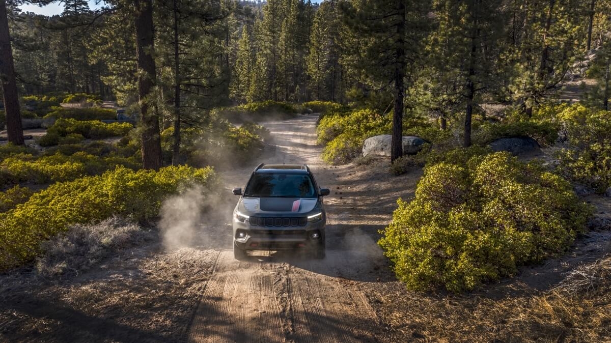 Jeep Compass roulant sur un chemin de terre dans une foret.