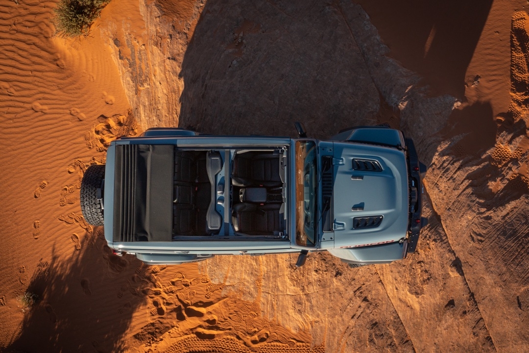 Vue aérienne du Jeep Wrangler 2025 décapotable avec toit souple ouvert, stationné sur un sol sablonneux.