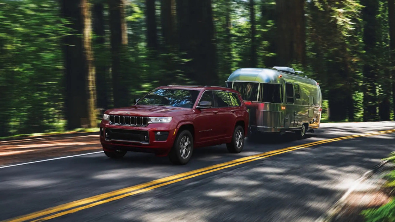 vue latérale avant d'un Jeep Grand Cherokee 2025 remorquant une roulotte sur une route en forêt