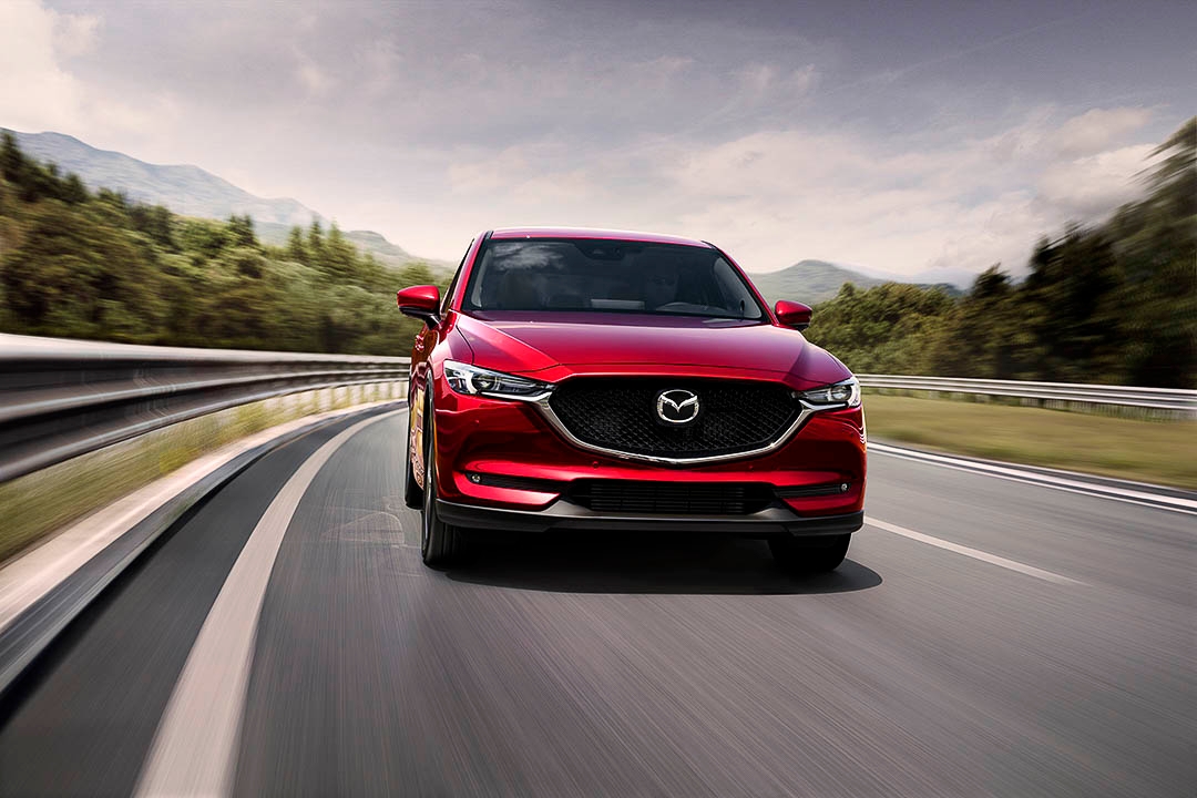 Mazda CX-5 2021 rouge roulant sur une autoroute sinueuse en montagne, vue frontale dynamique.