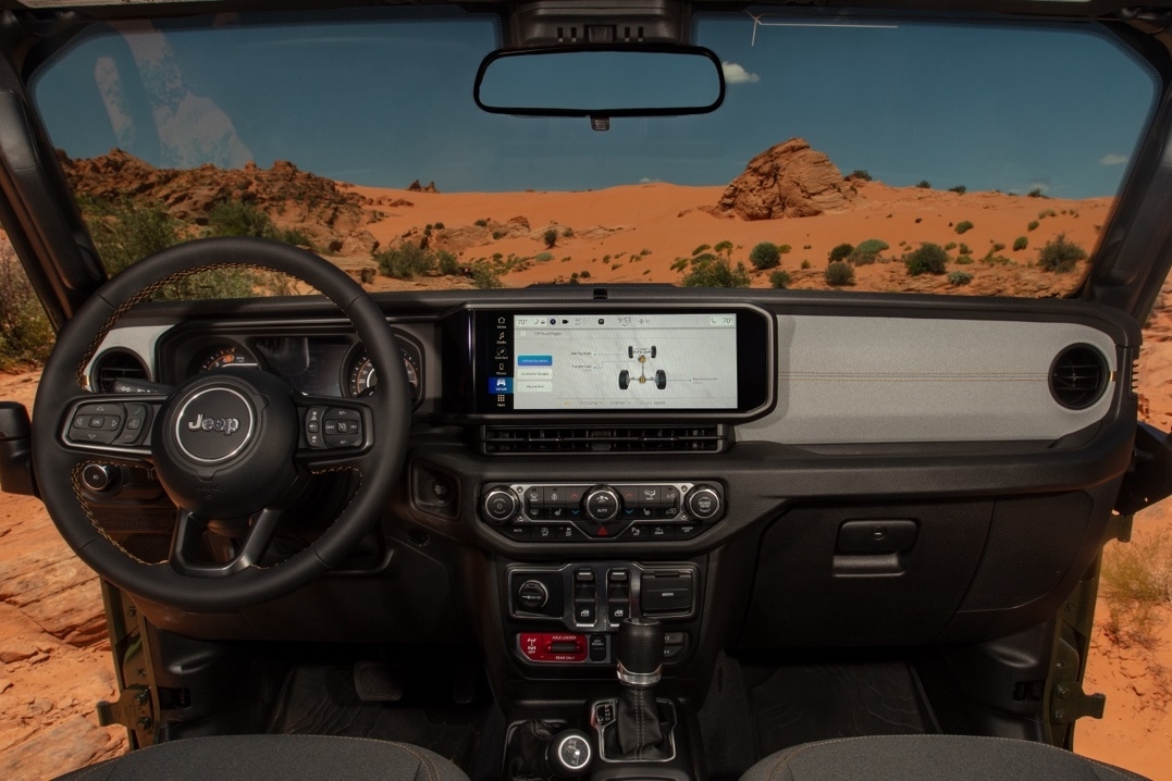 Tableau de bord du Jeep Wrangler 2025 avec écran Uconnect 5 affichant les modes 4x4, vu depuis l’intérieur en direction du désert.