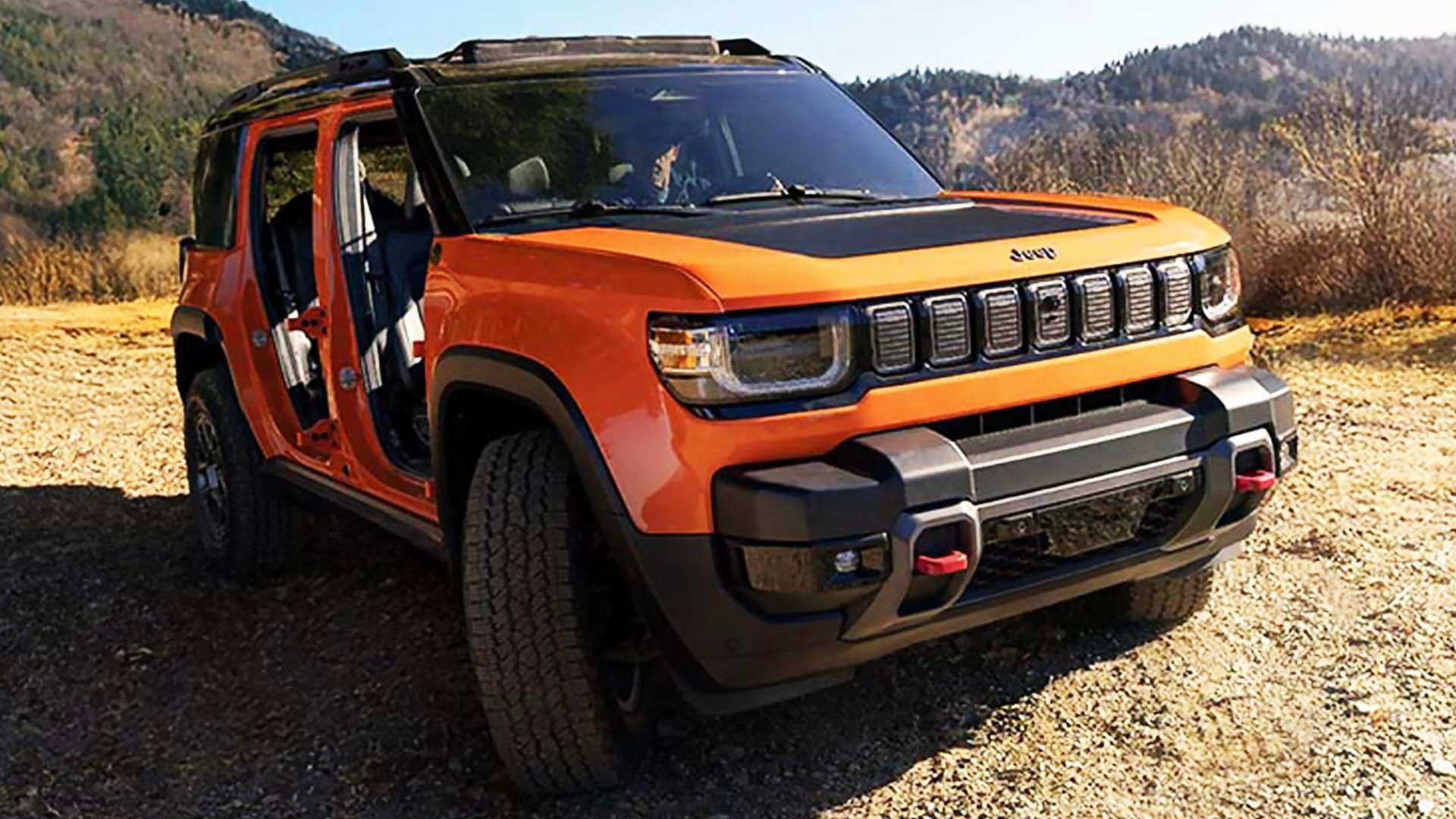 Jeep Recon 2026 orange sans portières garé sur chemin de terre, avec montagnes et végétation en arrière-plan.
