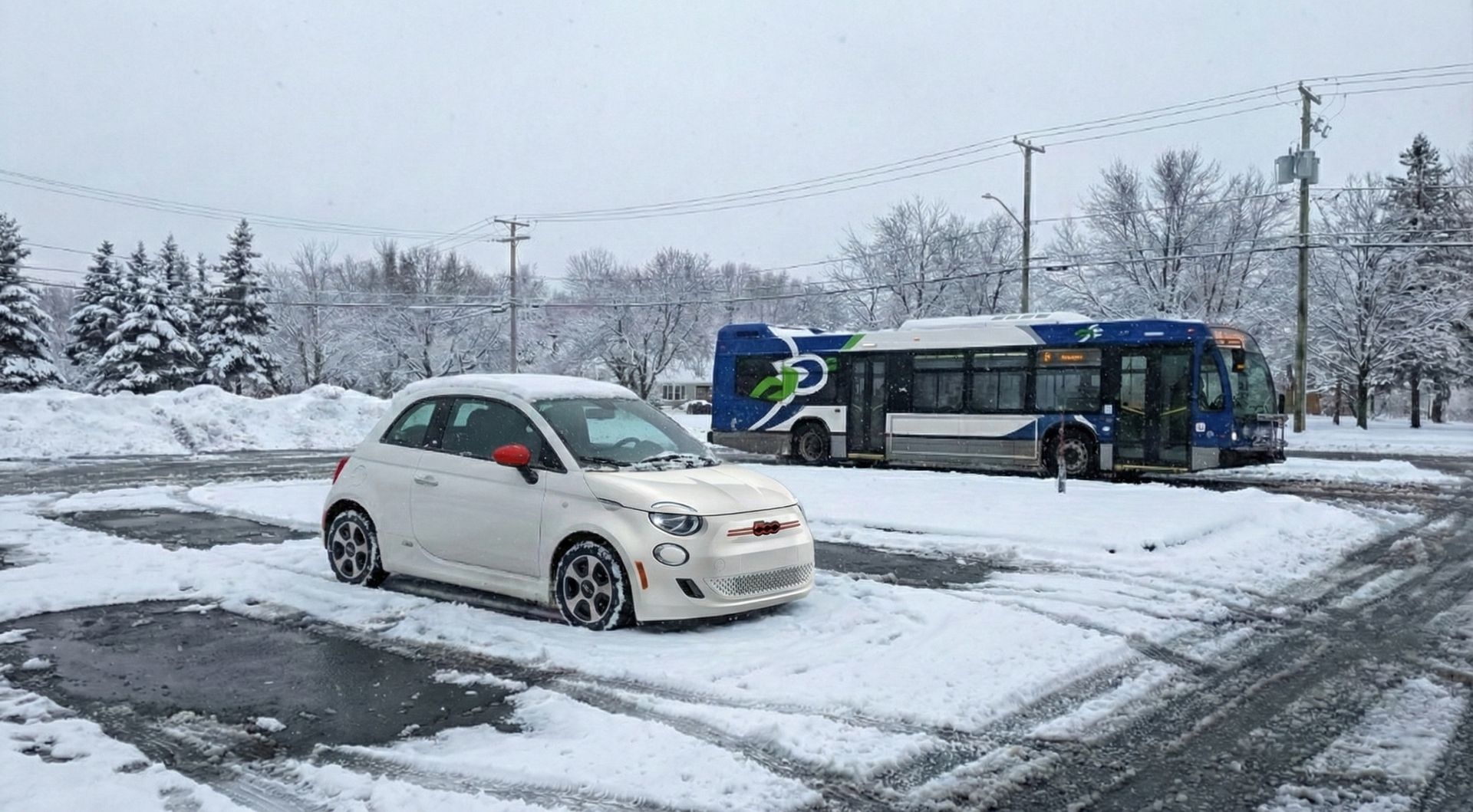 Fiat 500e blanche stationnée dans un Parc-O-Bus enneigé de Québec avec un autobus qui arrive en arrière-plan, illustrant la préparation d’une visite au marché de Noël