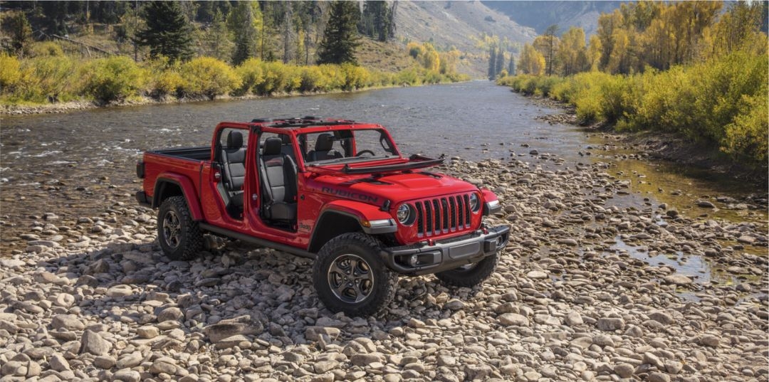 Jeep Gladiator stationné sur des petites roches au bord de la rivière.