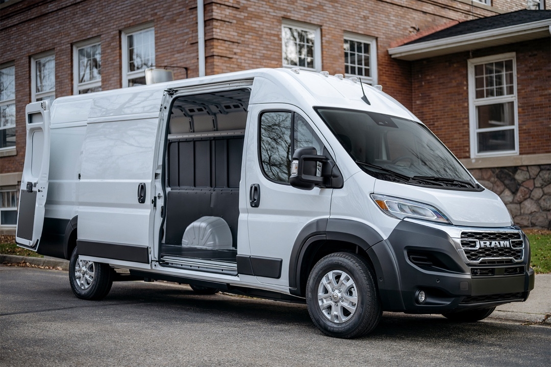 Ram ProMaster EV 3500 2025 blanc avec porte coulissante ouverte, garé en bordure d’un trottoir en ville.