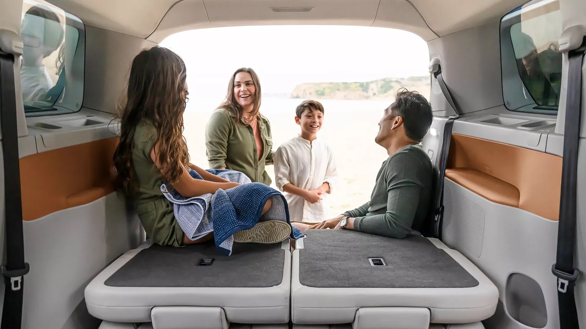 Volkswagen ID.Buzz 2025 vue de l’arrière avec une famille souriante installée à l’intérieur, hayon ouvert face à la plage.
