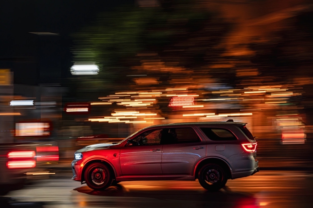 Vue latérale du Dodge Durango SRT Hellcat 2025 roulant à vive allure dans une rue urbaine éclairée.