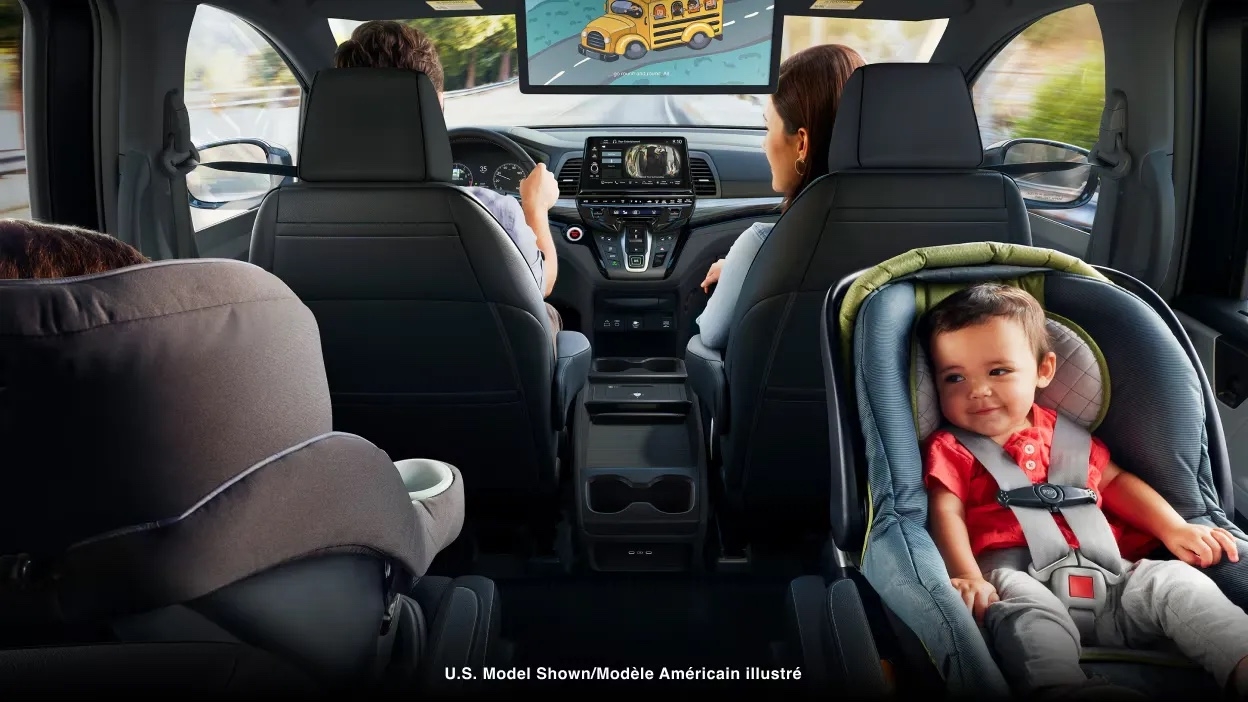 Habitacle de la Honda Odyssey 2025 vu de l’arrière, avec deux enfants en sièges d’auto et des écrans de divertissement installés au plafond.