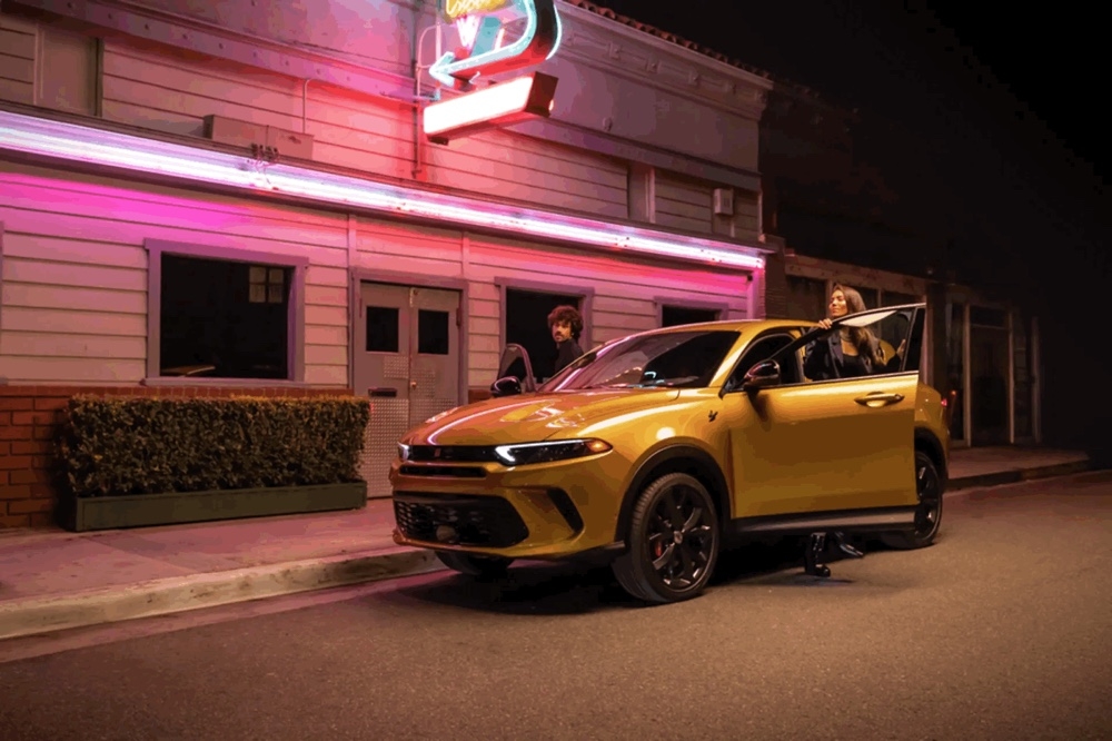 Dodge Hornet GT 2025 jaune stationné devant un restaurant rétro éclairé au néon rose en soirée.