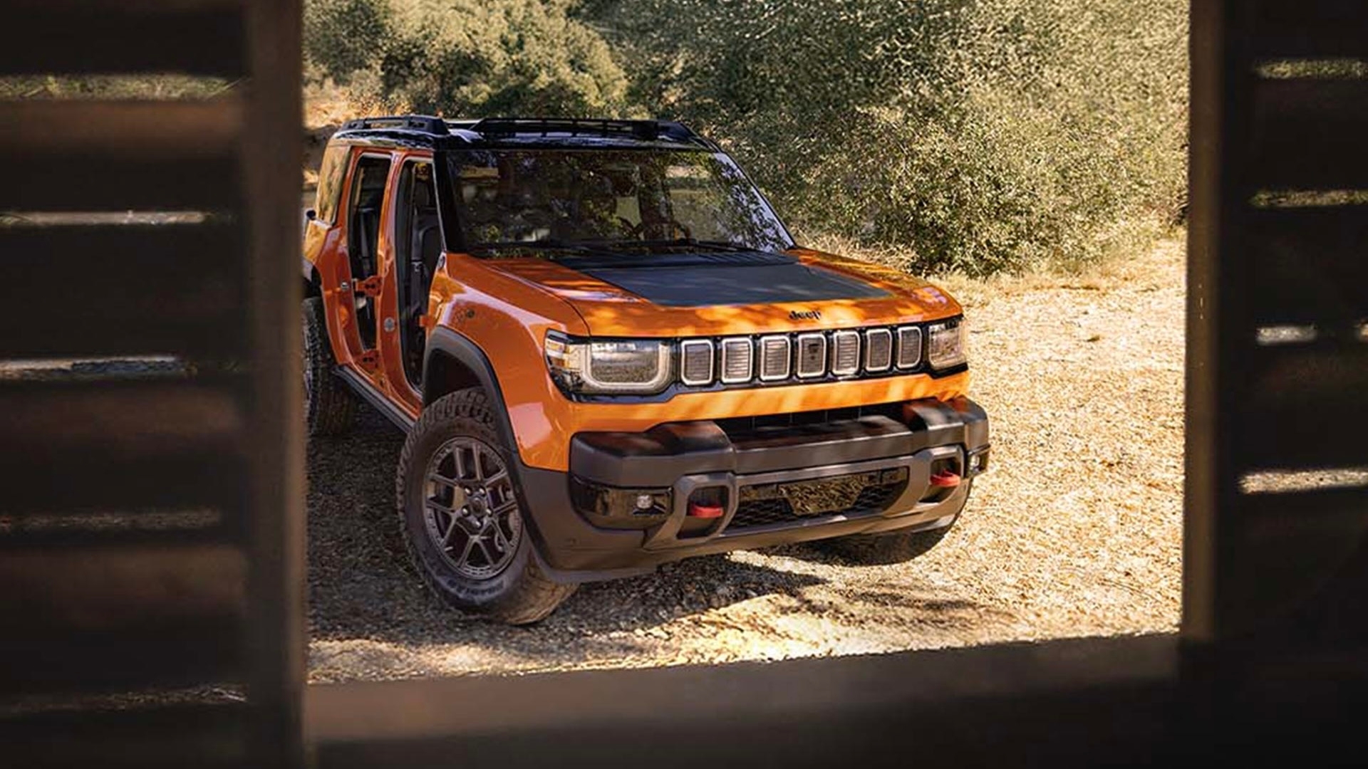 Jeep Recon 2026 vu à travers une fenêtre de cabane en bois, stationné en pleine nature avec portières ouvertes.