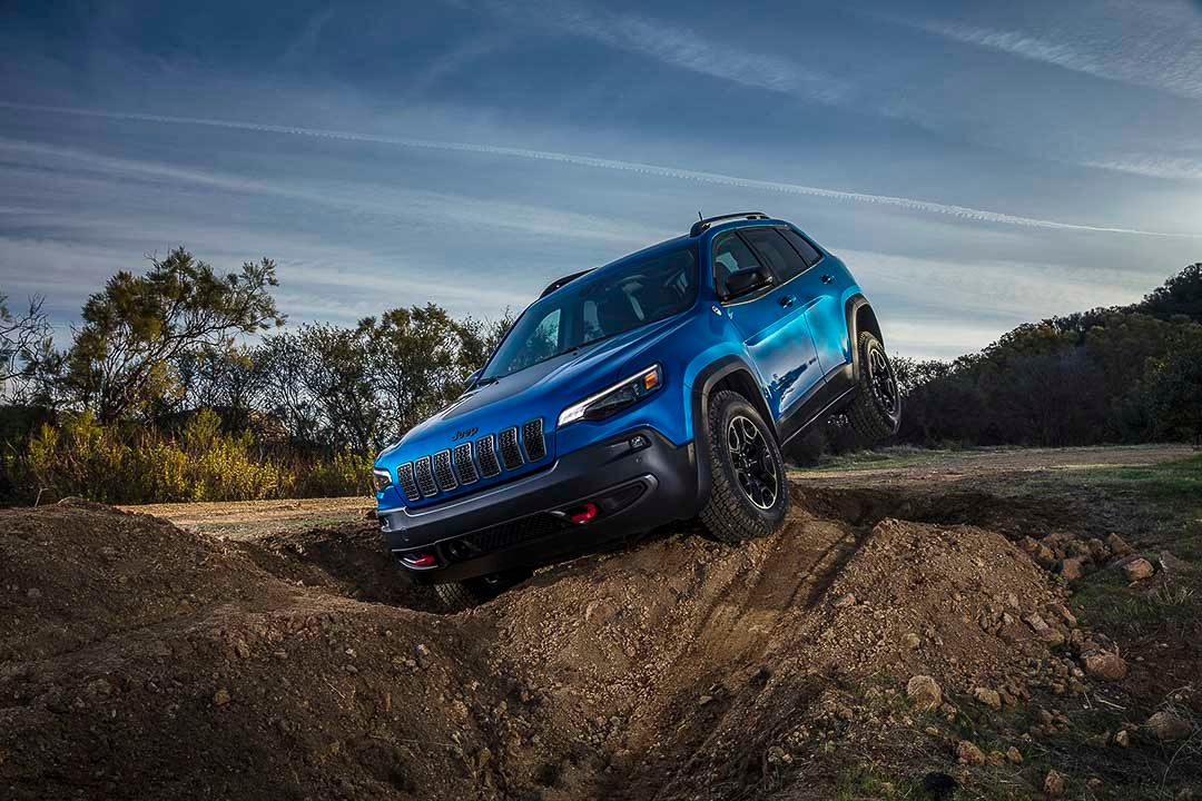 Jeep Cherokee Trailhawk 2021 bleu en action hors route sur un terrain accidenté, avec une roue avant levée.